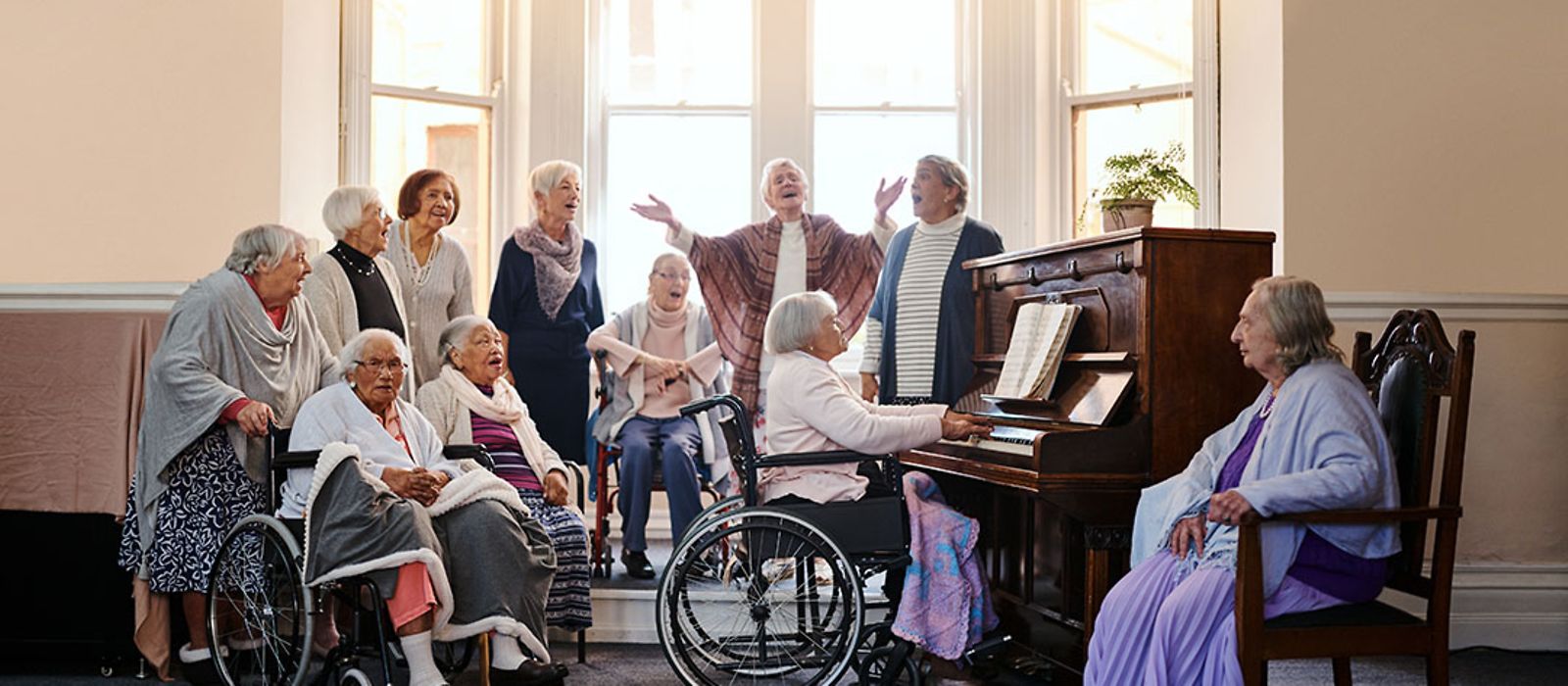 Eine Gruppe aus älteren Frauen singt gemeinsam im Chor, eine Frau sitzt am Klavier.