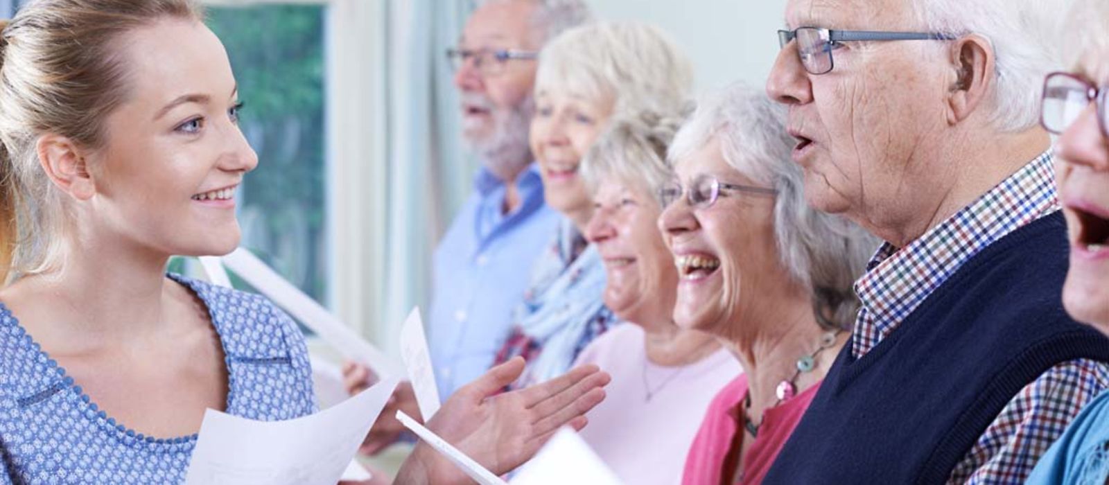 Eine Gruppe von Senioren mit der Lehrerin singen zusammen im Chor.